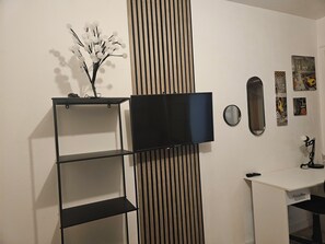 A room with a TV mounted on the wall, a wooden slat panel, a white desk, and a mirror. - Nice whole family/group apartment with free parking (Mérignac)