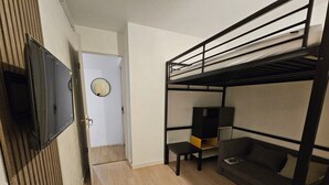 Une chambre avec un lit superposé, un téléviseur fixé au mur, une petite table et un canapé.