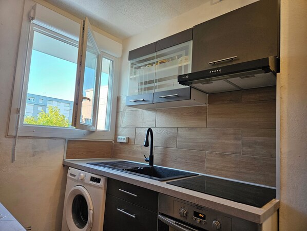 A compact kitchen with a washing machine, a stove, and a window with a view of buildings. - Nice whole family/group apartment with free parking (Mérignac)