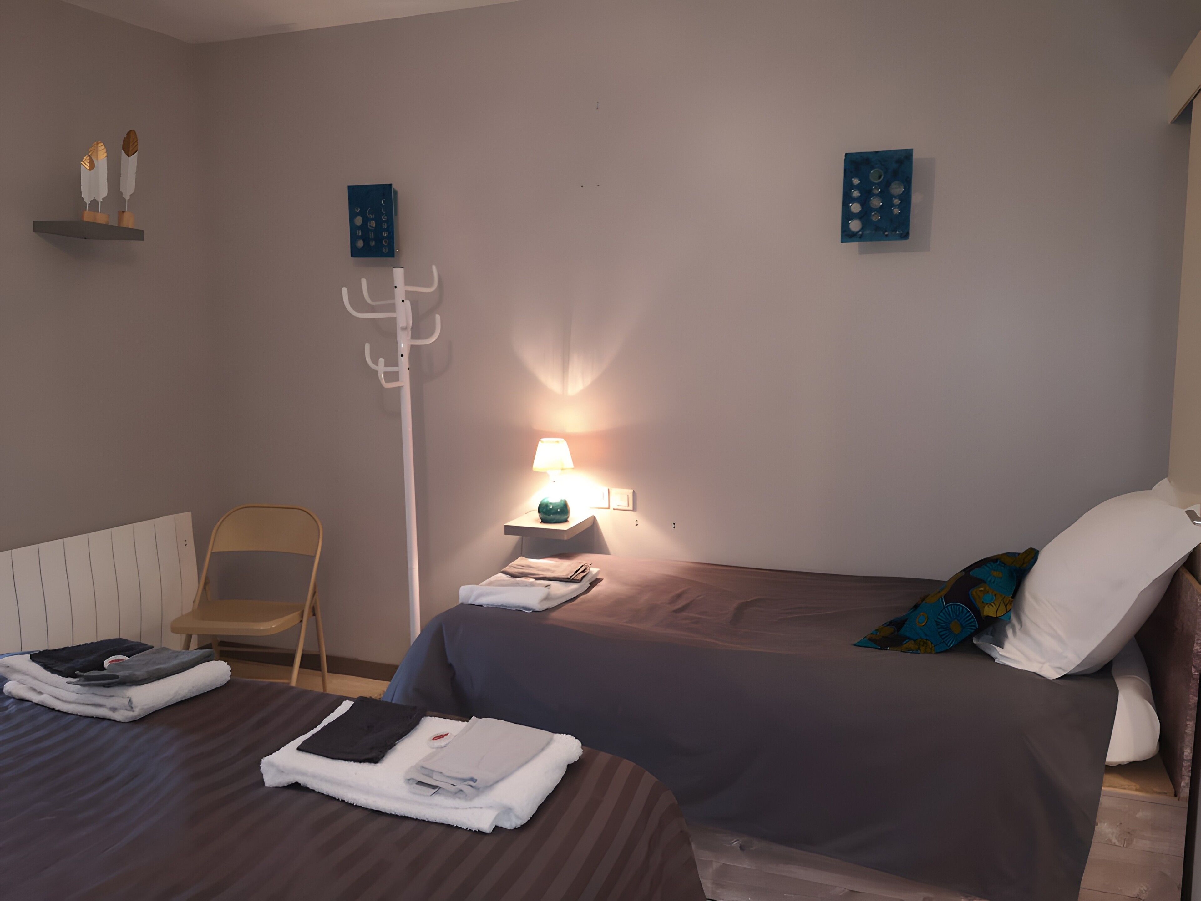 Un dormitorio con una cama, una silla, una mesita de noche con lámpara y obras de arte en las paredes.