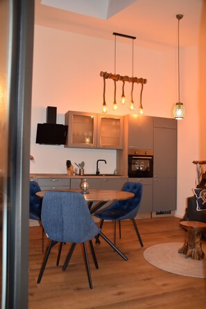 Une cuisine moderne avec un coin repas, comprenant un four encastré, un four à micro-ondes et un luminaire suspendu.