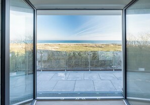 Une chambre moderne dotée de grandes fenêtres en verre offrant une vue sur la plage et la mer.