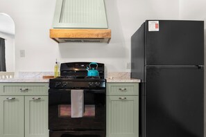 A kitchen with a black stove, teal kettle, and a black refrigerator.