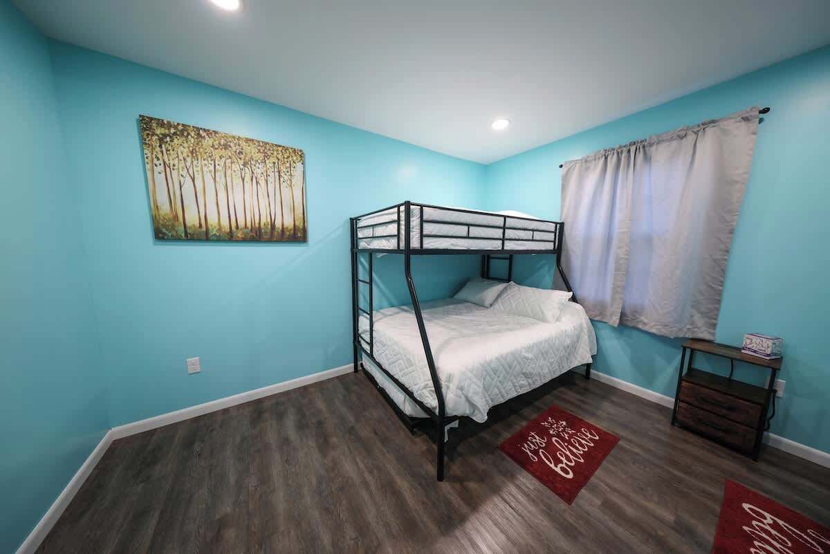 Une chambre avec un lit superposé, un mur bleu, un tableau et un tapis rouge.