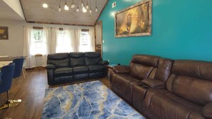 Uma sala de estar com parede azul, um sofá de couro marrom, um tapete estampado em azul e teto com vigas de madeira e iluminação embutida.
