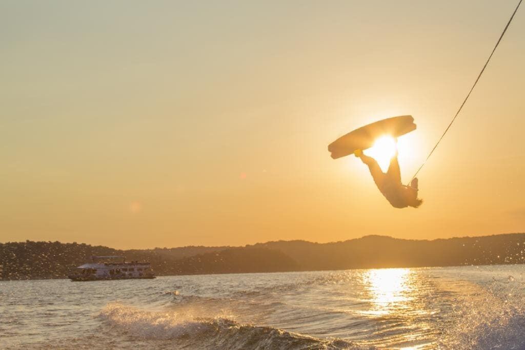 En person som åker wakeboard på vattnet med en båt i bakgrunden.