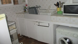 Ett kök med diskho, mikrovågsugn, tvättmaskin och ett fönster med persienner.
