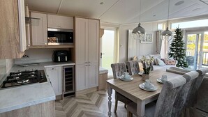 A modern kitchen with a gas stove, built-in oven, and microwave. There is a dining area with a wooden table and chairs, and a small Christmas tree. - Host & Stay | The White Swan (Allerthorpe)