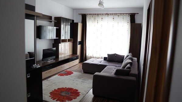 A modern living room with a flat-screen TV, built-in shelves, a sectional sofa, and a large window with curtains.