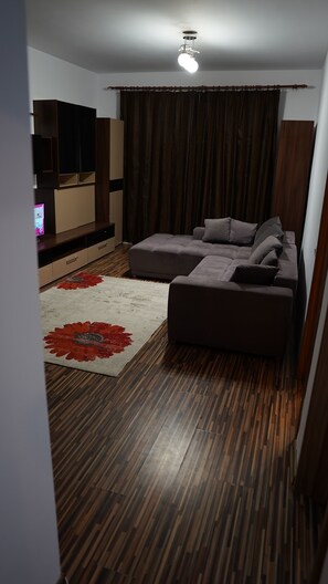 Una sala de estar con un sofá modular, un televisor de pantalla plana, piso de madera y un ventilador de techo.