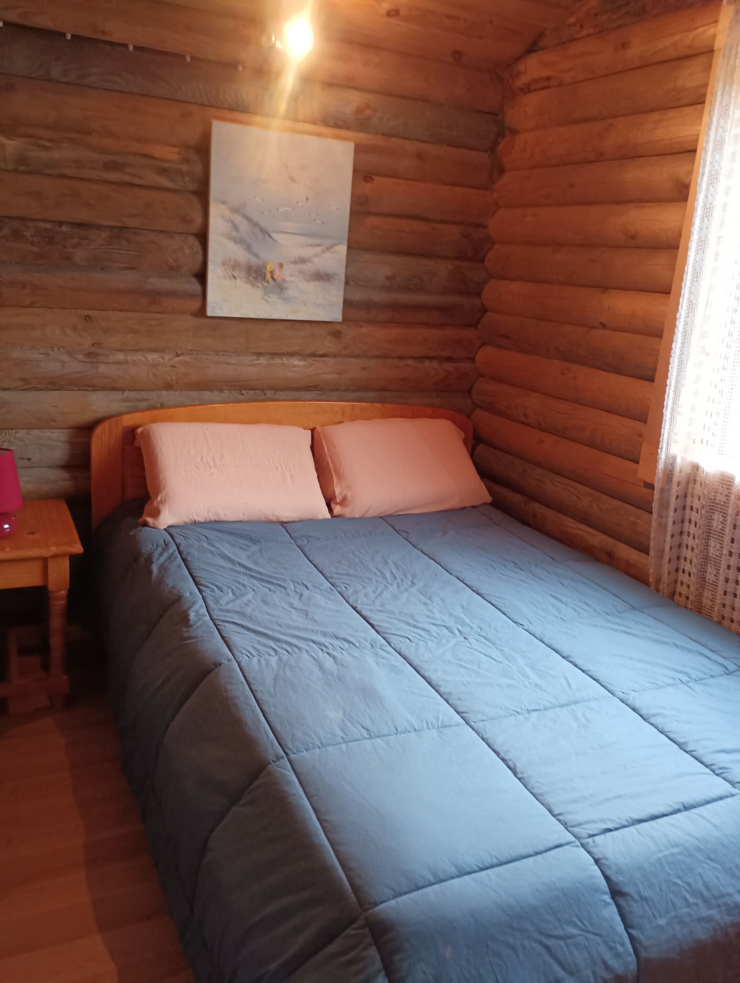 Una habitación tipo cabaña de madera con una cama, una mesita pequeña y un cuadro en la pared.