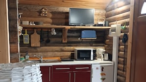 Cocina compacta con paredes de madera, microondas, un refrigerador pequeño y un estante de madera sobre la encimera.