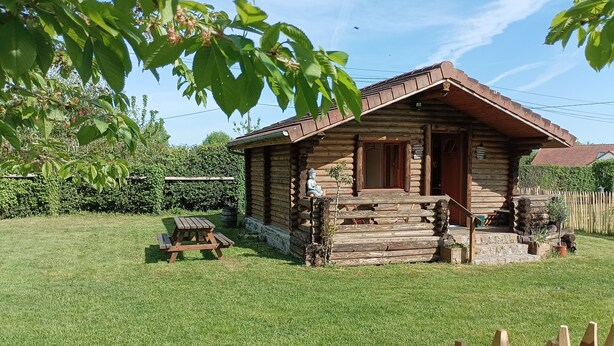 Una cabaña de troncos con un porche, una mesa de picnic y un patio cercado.