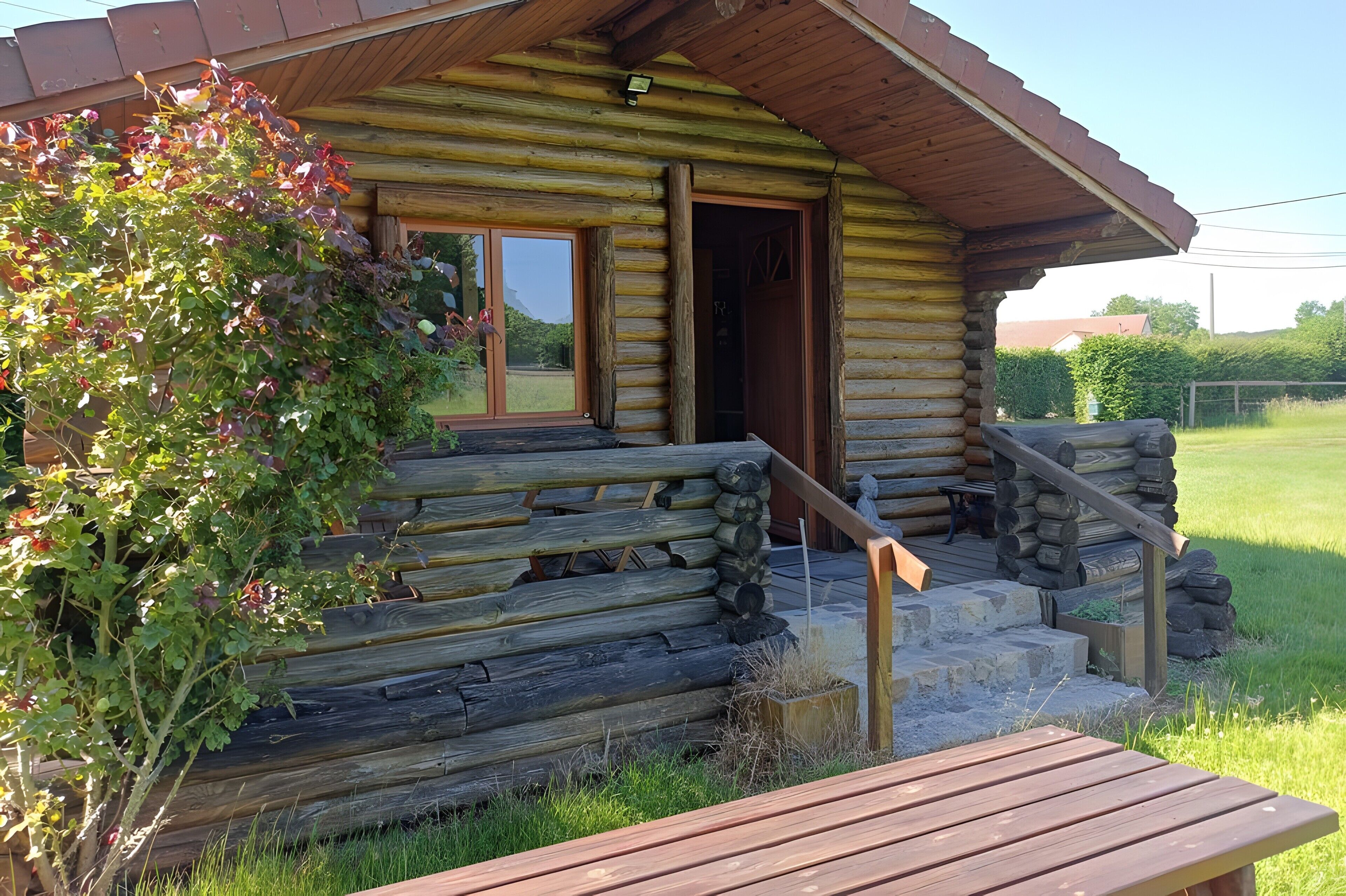 A log cabin with a wooden porch, a bench, and a small outdoor seating area.