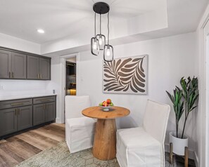 A modern kitchen with grey cabinets, a round wooden table, white chairs, and a decorative leaf painting. - Your Modern Scandinavian Escape/King Beds/Spa-Like Master Shower/Prime Dallas (Dallas)