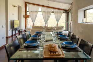 A dining area with a glass table set for six, black chairs, and a television in the background.