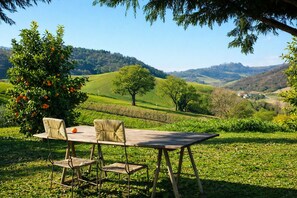 A wooden table with chairs in a grassy outdoor area with a view of rolling hills.