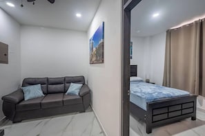 A modern bedroom with a dark leather sofa, a bed with a blue patterned bedspread, and a painting on the wall. - 17BR Jacó Retreat w/ Private Pool for Groups (Jaco)