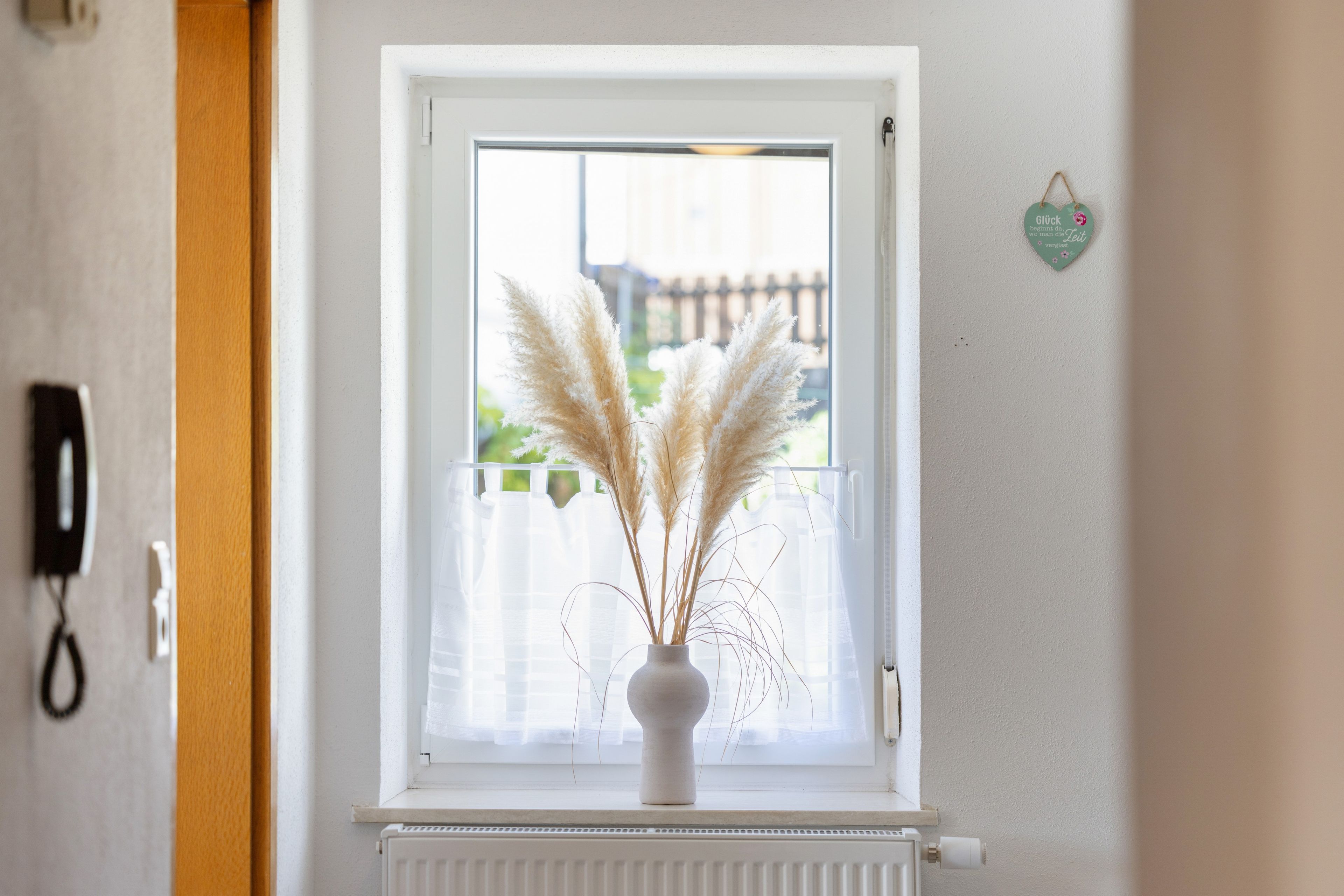 A window with a white frame, a white radiator below, and a vase with pampas grass on the sill.