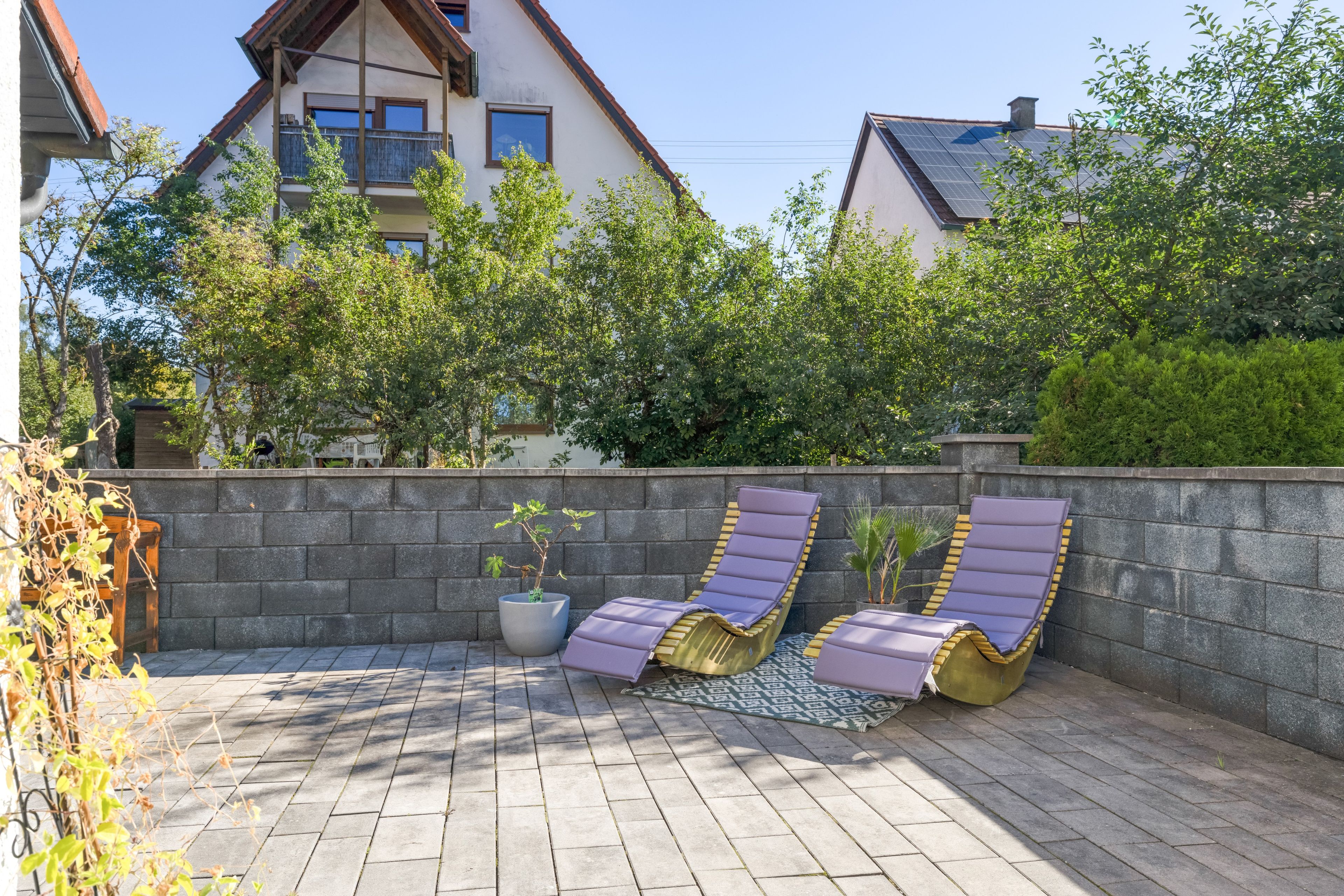 Eine Terrasse mit zwei Liegestühlen, einem Blumentopf und einer Steinmauer.