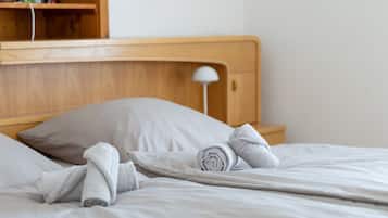 Ein ordentlich bezogenes Bett mit grauem Kopfkissen und zusammengerollten Handtüchern, ein Holz-Kopfbrett und eine Nachttischlampe.