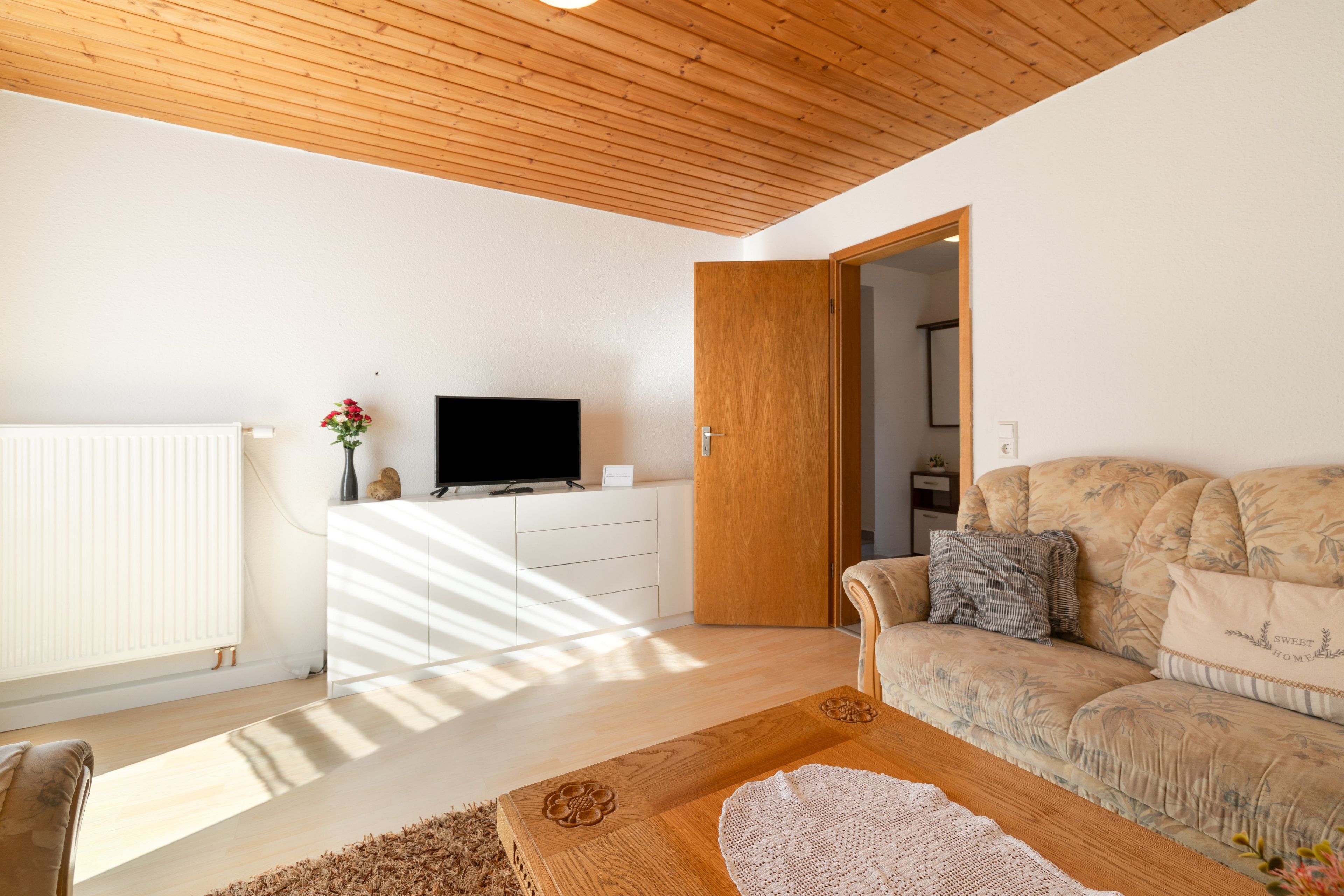 Una sala de estar moderna con un televisor de pantalla plana, techo de madera y un sofá con tapicería floral.