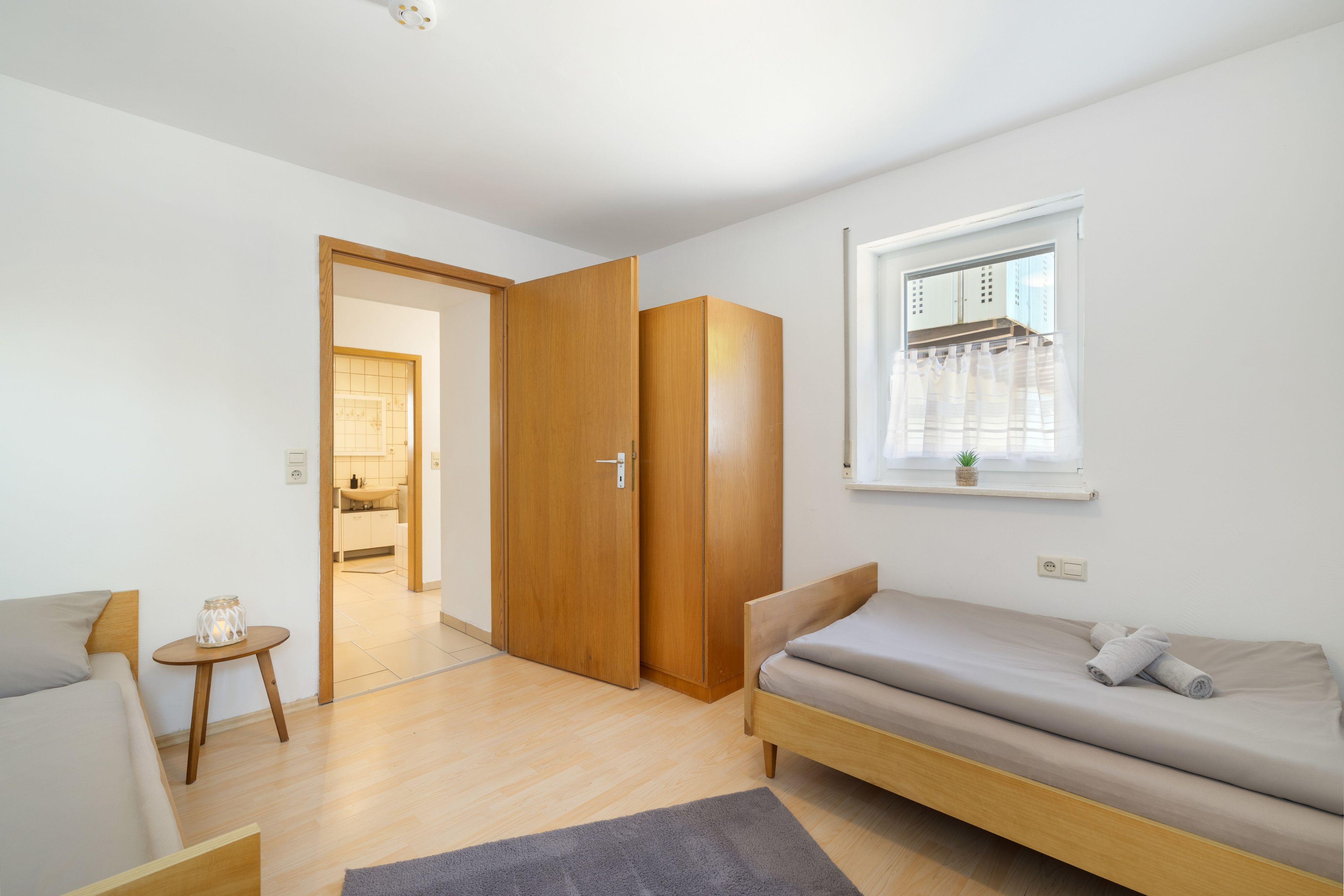 A modern, minimalistic bedroom with a wooden wardrobe, a single bed, and a small table with a lamp.