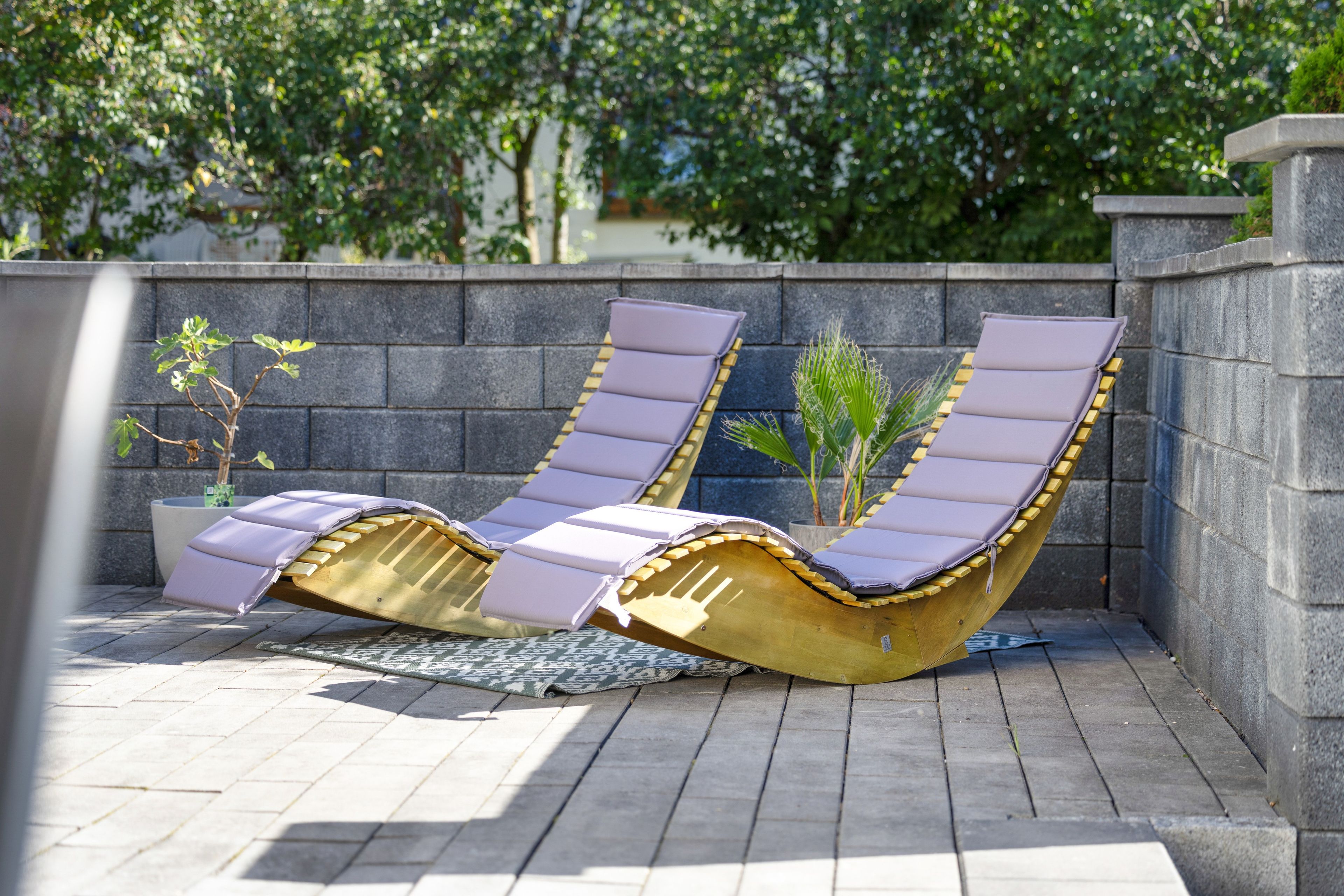 Deux chaises longues avec des coussins, une plante en pot et un tapis à motifs sur une terrasse carrelée.