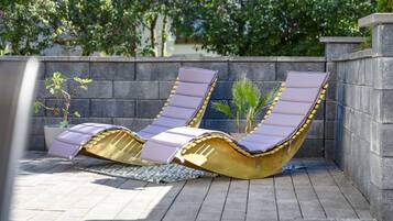 Deux chaises longues avec des coussins, une plante en pot et un tapis à motifs sur une terrasse carrelée.