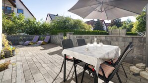 En udendørs patio med et bord, stole og en stor parasol, samt en stenvæg.