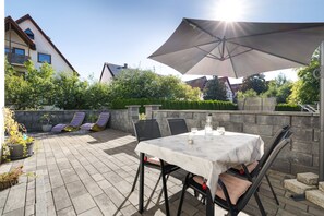 Een terras buiten met een tafel, stoelen, een grote parasol en een stenen muur.