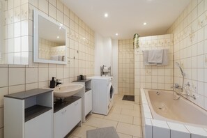 Een moderne badkamer met een wastafel, spiegel, wasmachine en bad.