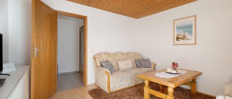 A room with a wooden ceiling, a sofa, a table with a placemat, and a framed picture on the wall.
