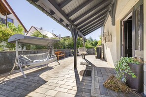 Un espacio al aire libre techado con una mecedora, un banco y una silla colgante.