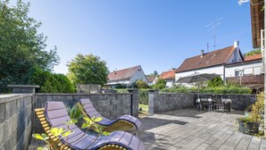 En patio med liggestole, en stenvæg og udsigt til huse i baggrunden.