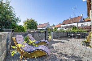 Een terras met lounge stoelen, een stenen muur en een uitzicht op huizen op de achtergrond.