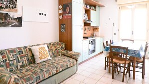 Un espacio habitable compacto con sofá, mesa de comedor, sillas, kitchenette y una puerta.