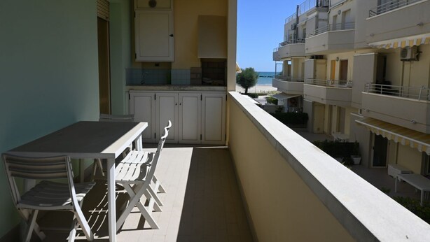 Un balcón con mesa y sillas, vista al mar, y un edificio con balcones.