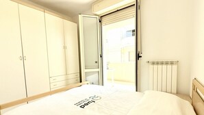 Un dormitorio con cama, armario, radiador y puerta que da a un balcón exterior.