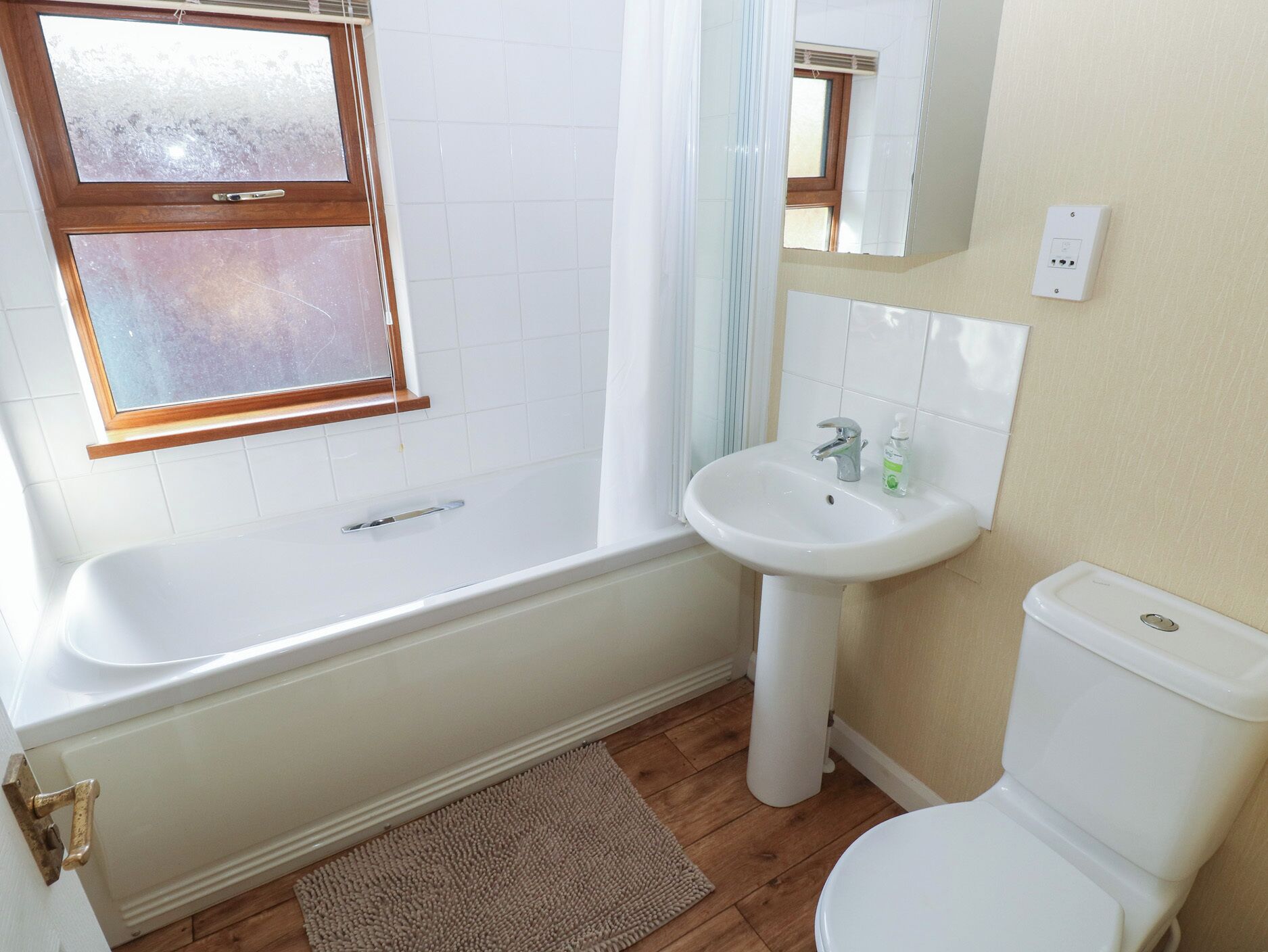 A bathroom with a bathtub, sink, toilet, and a window with frosted glass.