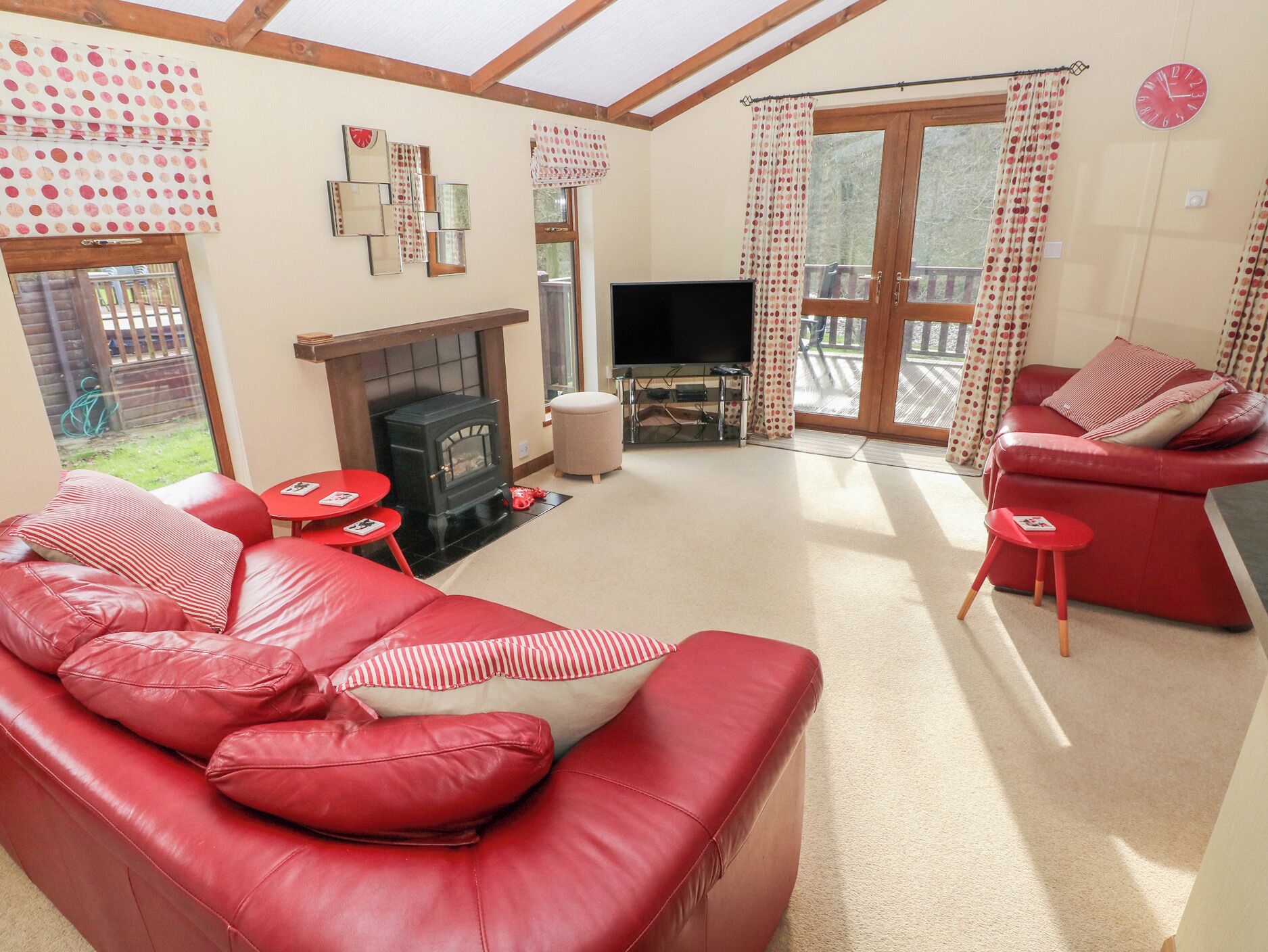 A living room with a red sofa, a fireplace, a television, and a balcony with curtains.