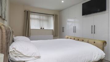 A bedroom with a bed, a radiator, a window with blinds, a television on the wall, and a wardrobe.