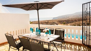 Une table dressée pour quatre personnes, avec vue sur la mer, une balustrade de balcon et un sol à motifs.