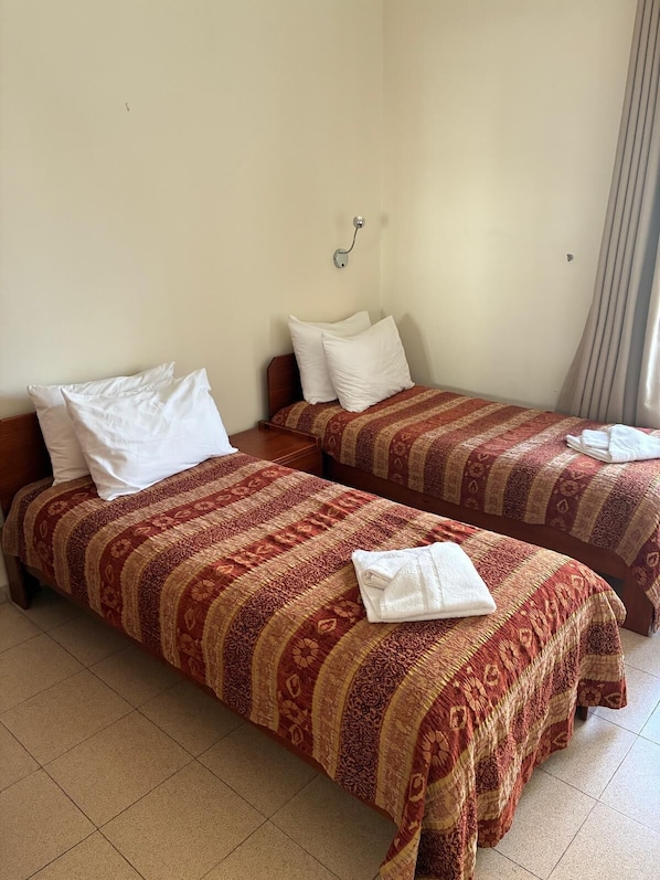 A hotel room with two beds, each with a patterned bedspread and white pillows. - Christ Church Guest House (Jerusalem)