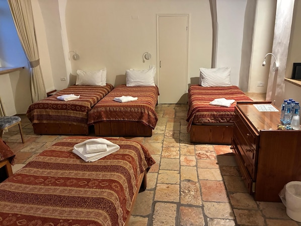 Ett hotellrum med tre sängar, en byrå i trä och ett klinkergolv.