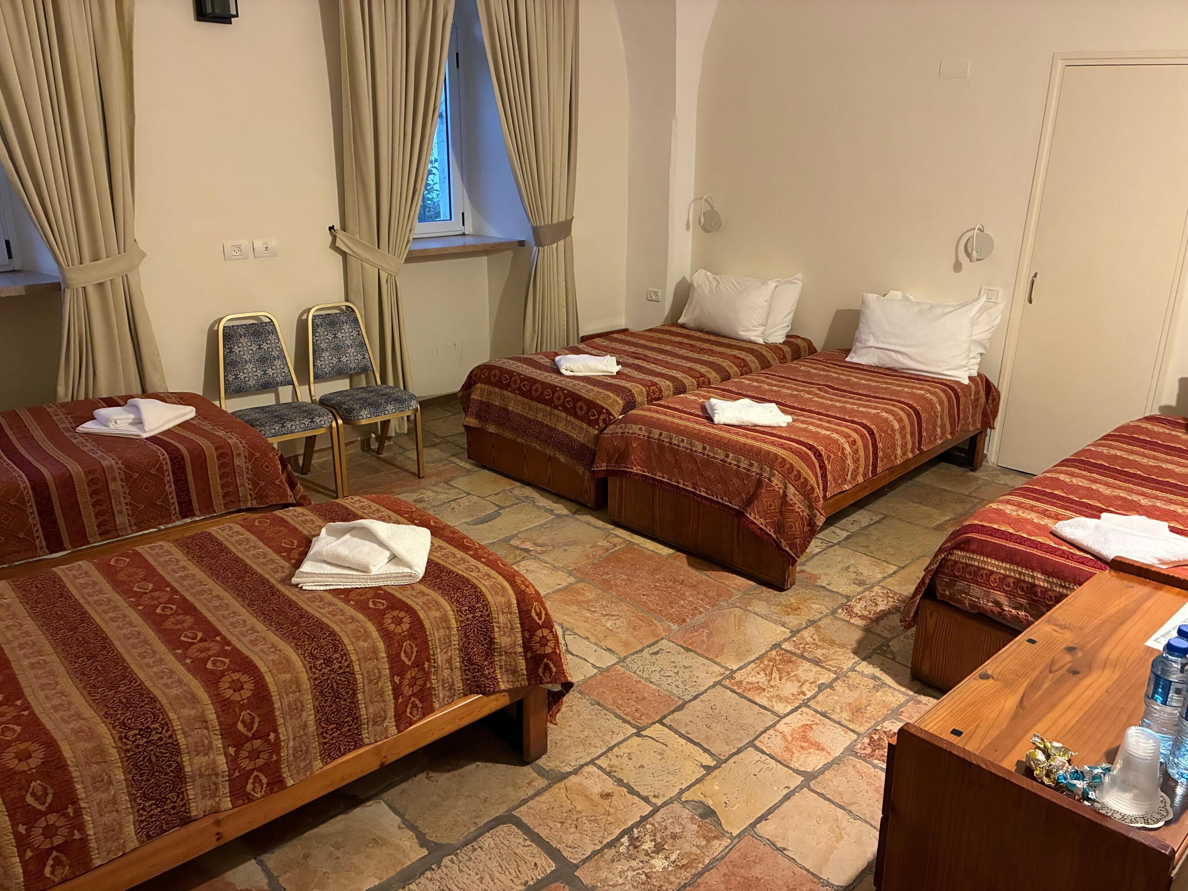 Une chambre d’hôtel avec trois lits, un bureau en bois, une chaise et une fenêtre avec des rideaux.