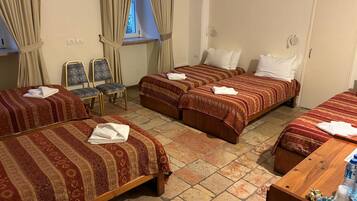 Une chambre d’hôtel avec trois lits, un bureau en bois, une chaise et une fenêtre avec des rideaux.