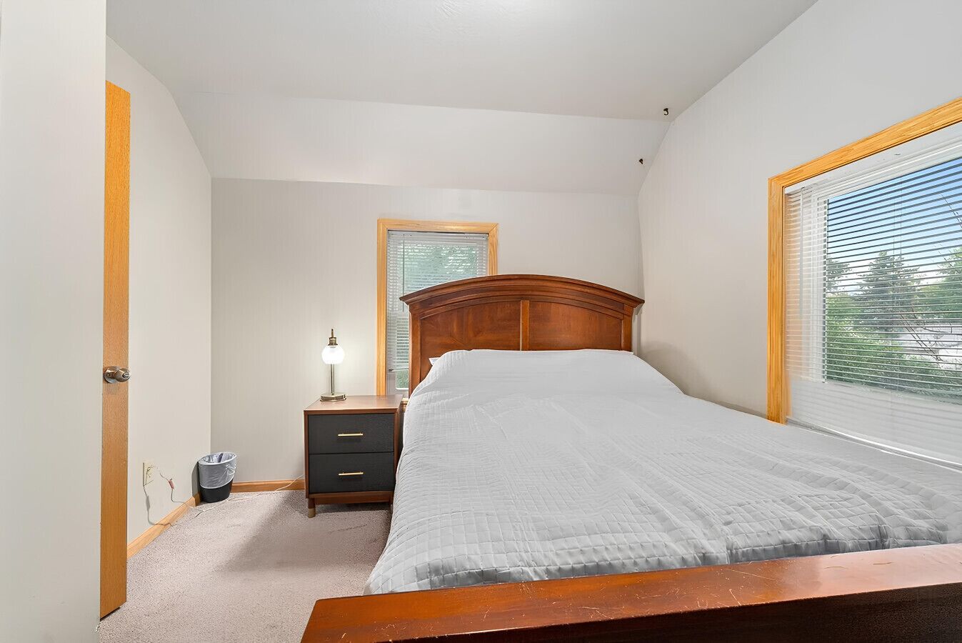 A bedroom with a bed, a nightstand, a lamp, a window, and a door.