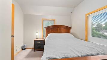 A bedroom with a bed, a nightstand, a lamp, a window, and a door.