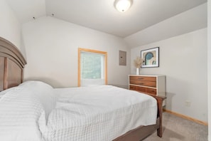 Un dormitorio con cama, cómoda, ventana con persianas, lámpara de techo e imagen enmarcada en la pared.